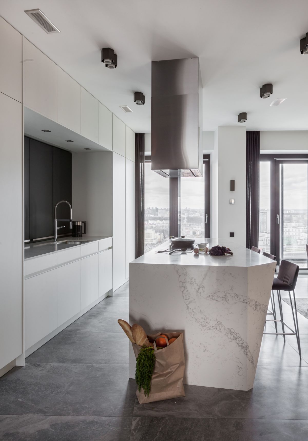 The kitchen is almost entirely white and has a massive and elegant island made from white marble